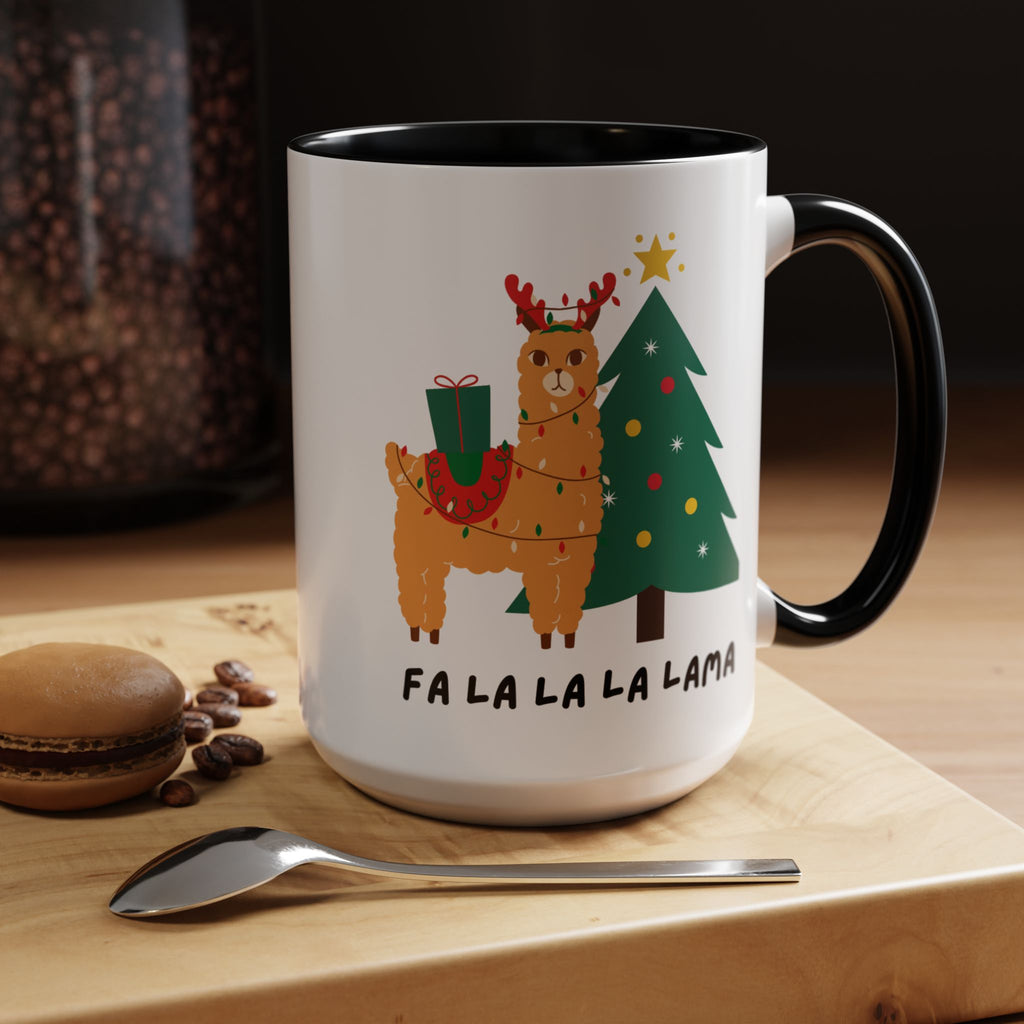 A white ceramic coffee mug with a black handle and interior, featuring a festive llama and Christmas tree illustration with the text 'FA LA LA LA LAMA'. The mug is styled on a wooden cutting board with a spoon, coffee beans, and a macaron.