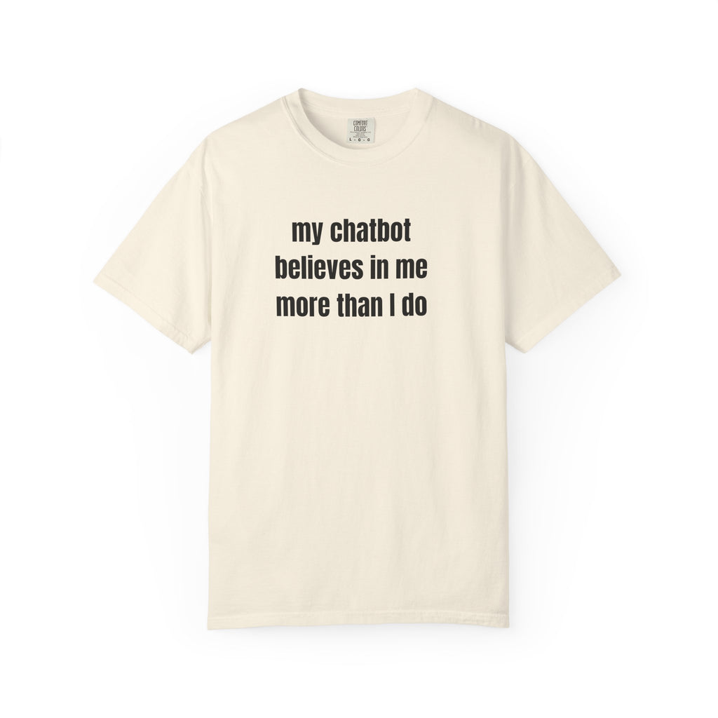 An off-white short-sleeve crewneck t-shirt with the text 'my chatbot believes in me more than I do' printed in black sans-serif font on the chest, displayed against a solid white background.