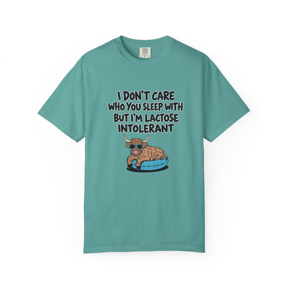 A teal short-sleeve t-shirt with a graphic print on the front. The graphic features a cartoon Highland cow sitting in a blue bathtub, with the text 'I DON'T CARE WHO YOU SLEEP WITH BUT I'M LACTOSE INTOLERANT' in black lettering.
