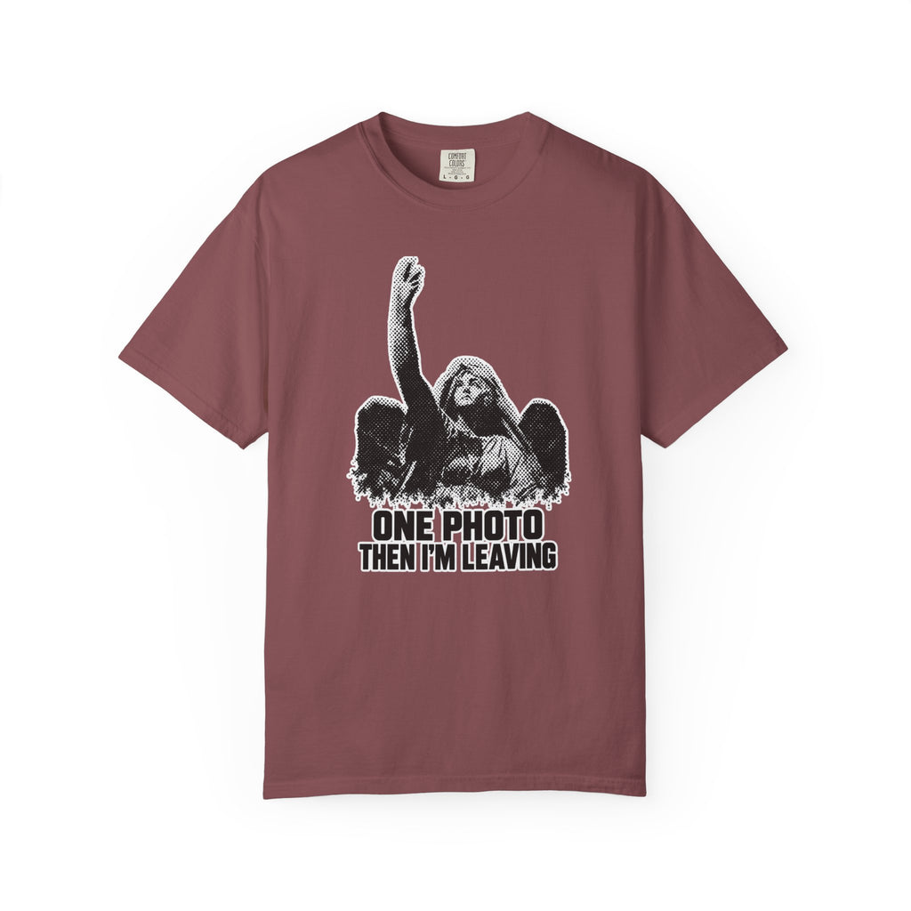 A short-sleeve crewneck t-shirt in a dusty rose or mauve color, featuring a black and white graphic of an angel with one arm raised and the text 'ONE PHOTO THEN I'M LEAVING' printed below.
