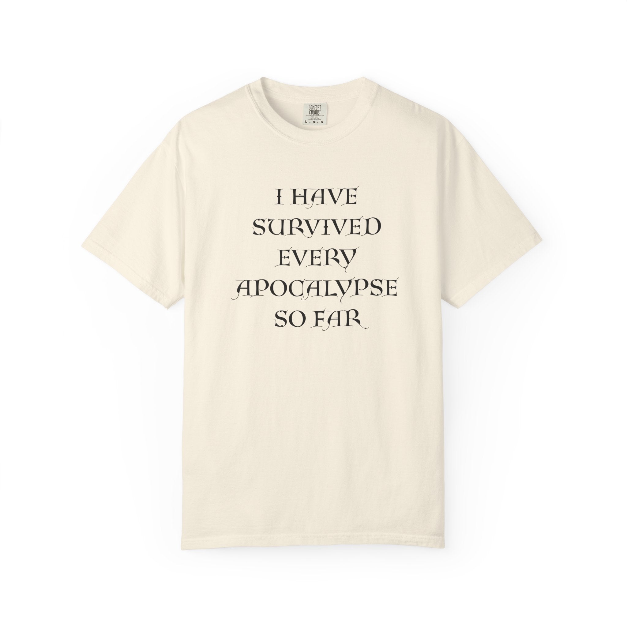 An off-white short-sleeve t-shirt with black text on the front reading 'I HAVE SURVIVED EVERY APOCALYPSE SO FAR', displayed against a solid white background.

