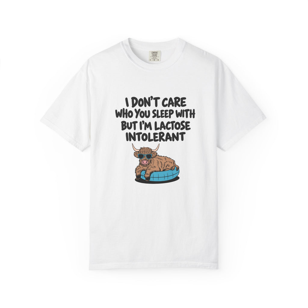 A white short-sleeve crewneck t-shirt featuring a humorous graphic print. The print displays the text 'I DON'T CARE WHO YOU SLEEP WITH BUT I'M LACTOSE INTOLERANT' in a bold black font above an illustration of a brown Scottish Highland cow lying on a blue pet bed.
