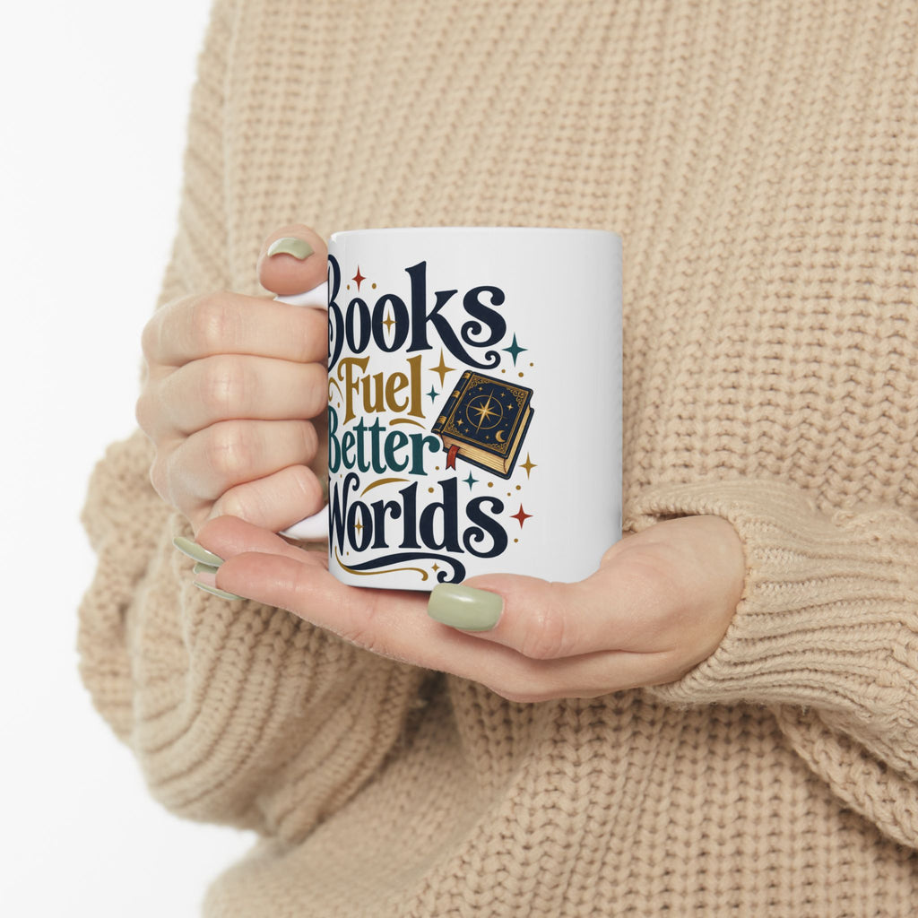 A person in a beige knit sweater holds a white ceramic mug with the phrase 'Books Fuel Better Worlds' in dark blue and gold lettering, alongside a small illustrated book.