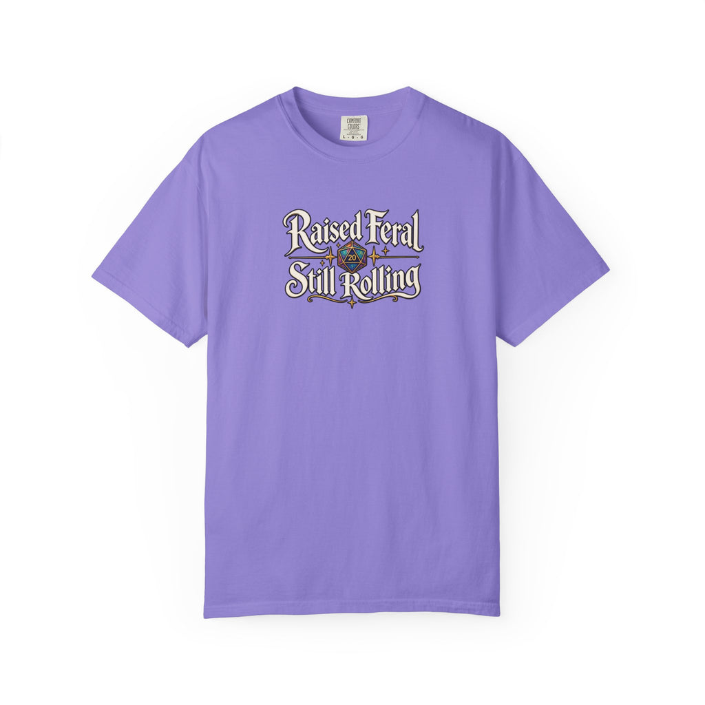 A purple graphic T-shirt  that features the text 'Raised Feral Still Rolling' with a colorful 20-sided die graphic in the center against a white background