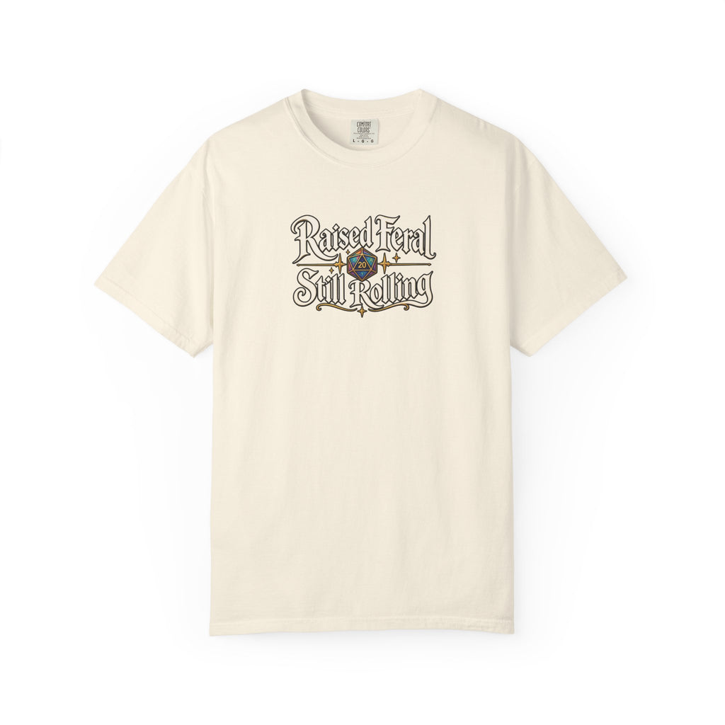 A beige graphic T-shirt  that features the text 'Raised Feral Still Rolling' with a colorful 20-sided die graphic in the center against a white background