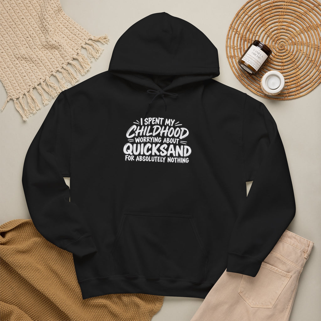 black hoodie with white text that reads: I SPEND MY CHILDHOOD WORRYING ABOUT QUICKSAND FOR ABSOLUTELY NOTHING. it is displayed with a beige knitted scarf and a candle