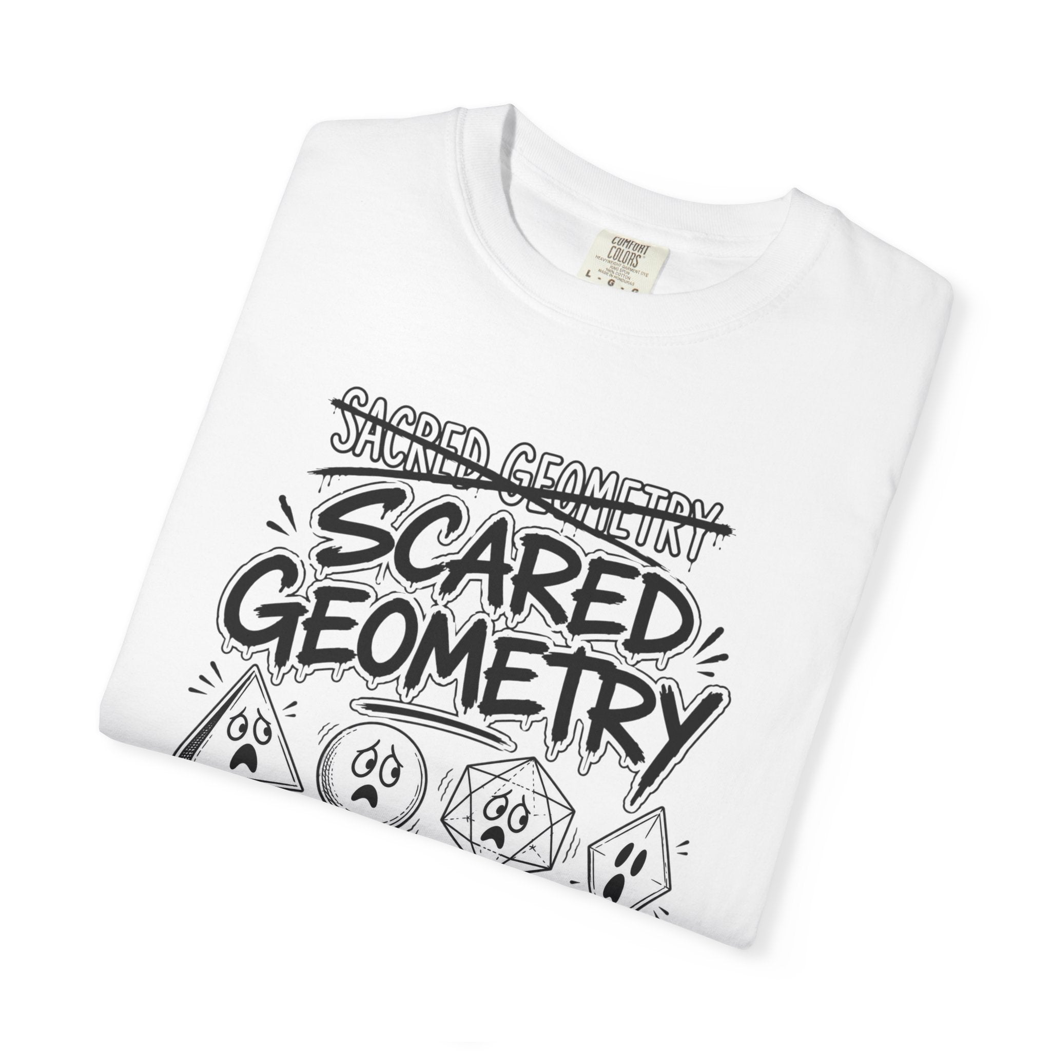 A folded white t-shirt with a black graphic that reads 'Sacred Geometry' crossed out above 'Scared Geometry,' featuring spooky-faced dice and geometric shapes, styled flat on a white surface.