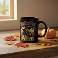 Black mug with a colorful graphic depicting a witch holding a green alien with the words: My familiar is an alien