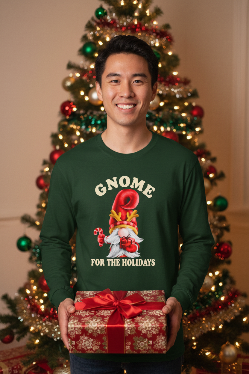 A man wearing a dark green long-sleeve Christmas sweater with a gnome graphic and the text 'GNOME FOR THE HOLIDAYS' holds a wrapped red gift box in front of a decorated Christmas tree