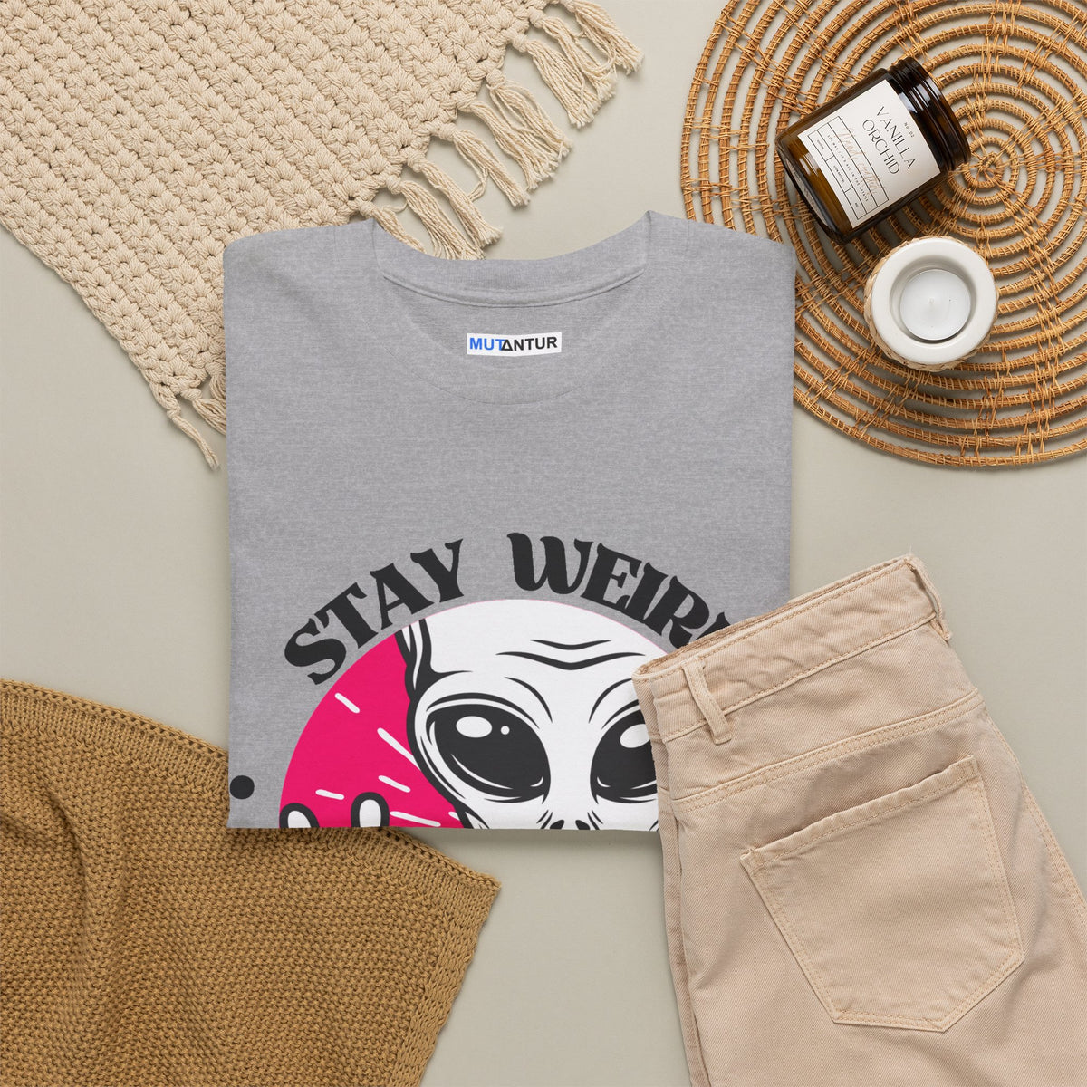 Stay Weird Stay Peaceful galaxy alien graphic tee in heather grey, folded flat lay styled with a woven placemat and tan trousers
