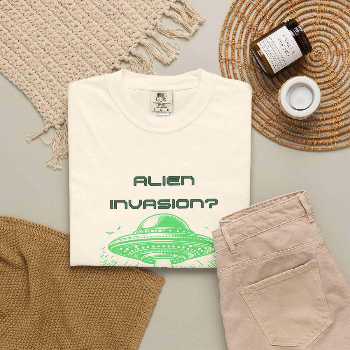Alien Invasion Finally New Management UFO graphic tee in cream, folded flat lay styled with a knit throw, candle, and khaki pants