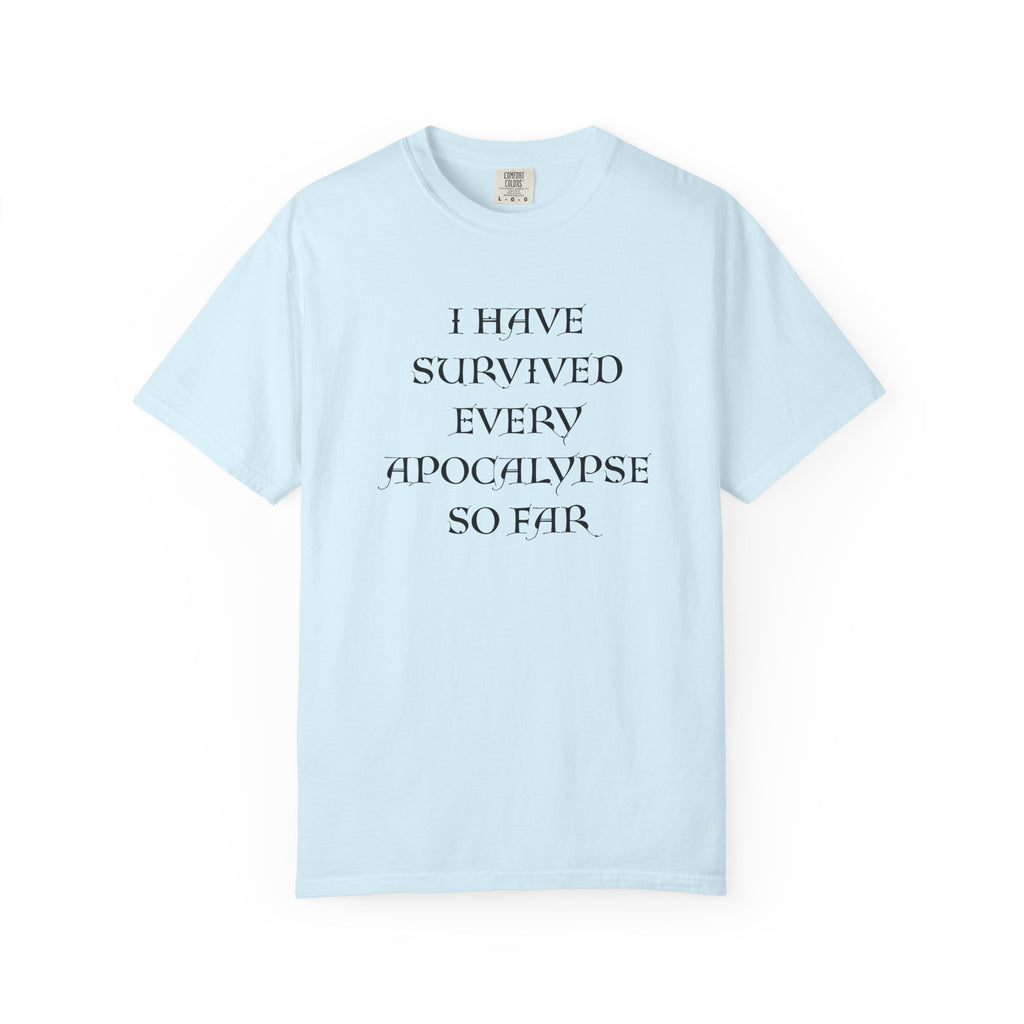A light blue short-sleeve crewneck t-shirt with the text 'I HAVE SURVIVED EVERY APOCALYPSE SO FAR.' printed in black serif font on the chest, displayed against a solid white background.