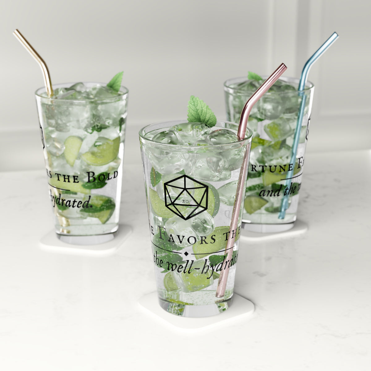 Three clear glass tumblers with metal straws on white coasters, filled with iced drinks and mint leaves, on a light marble-like surface.
