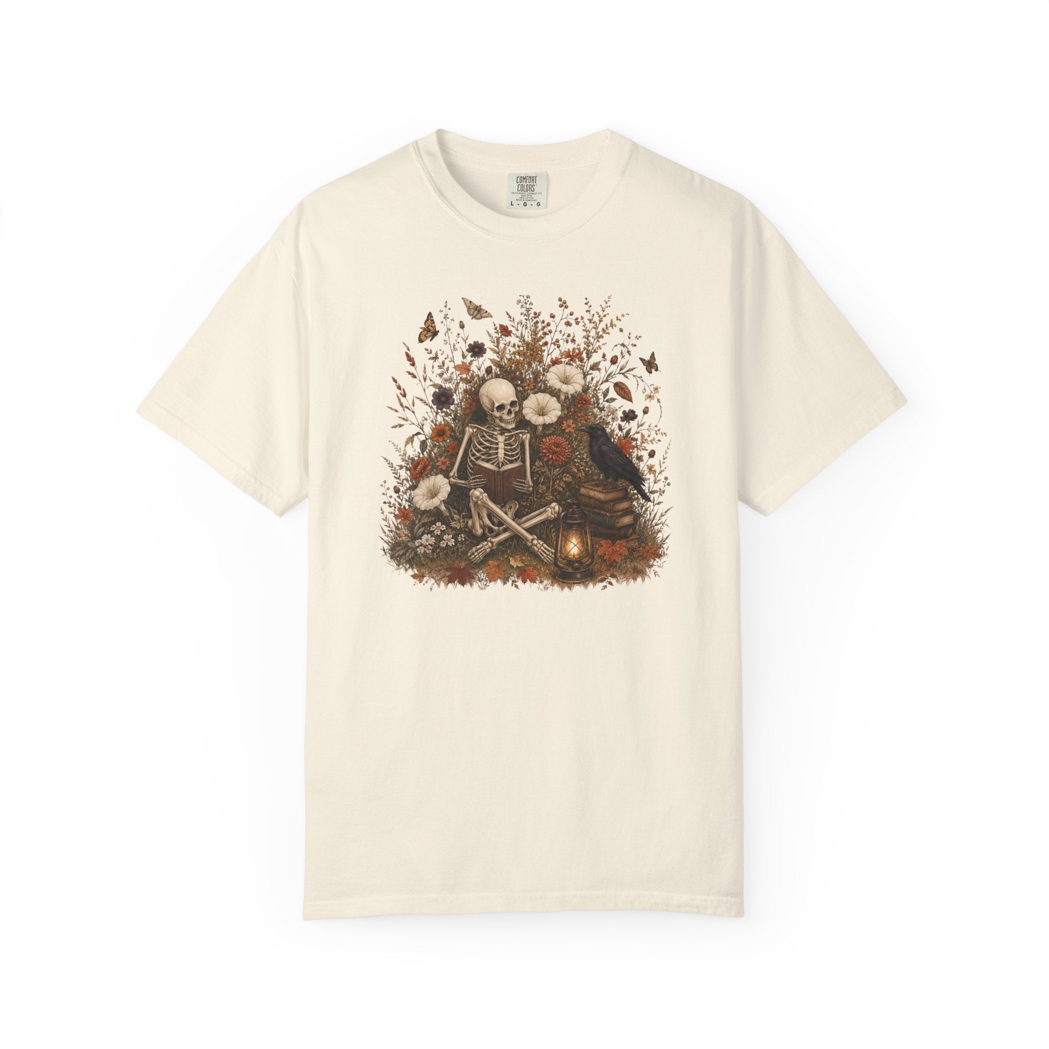 An off-white short-sleeve crewneck t-shirt featuring a central graphic print of a skeleton sitting among autumn leaves, skulls, and a small glowing candle.