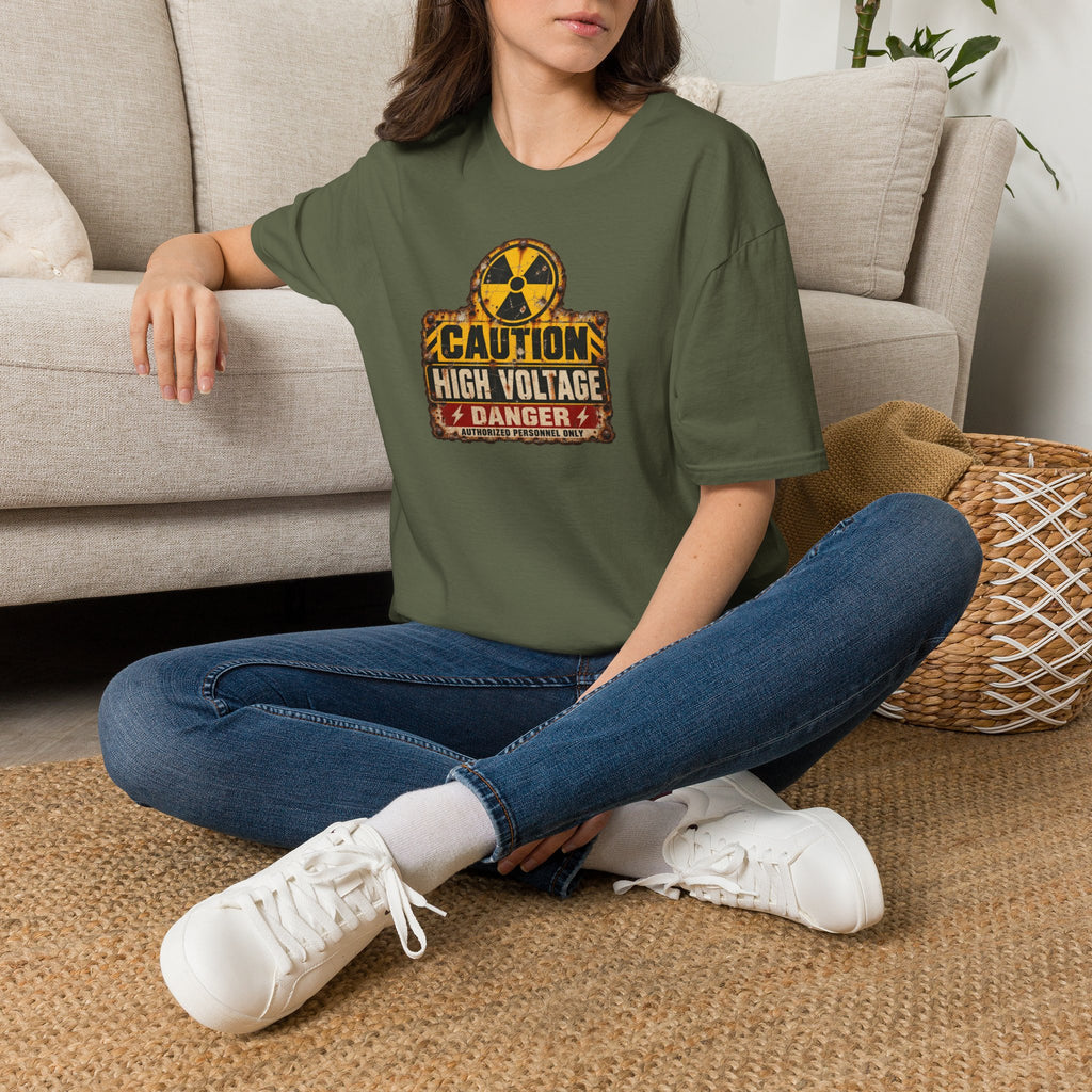 A sitting woman wearing a military green t-shirt with a distressed yellow, black, and red 'High Voltage' and Danger warning sign graphic on the front