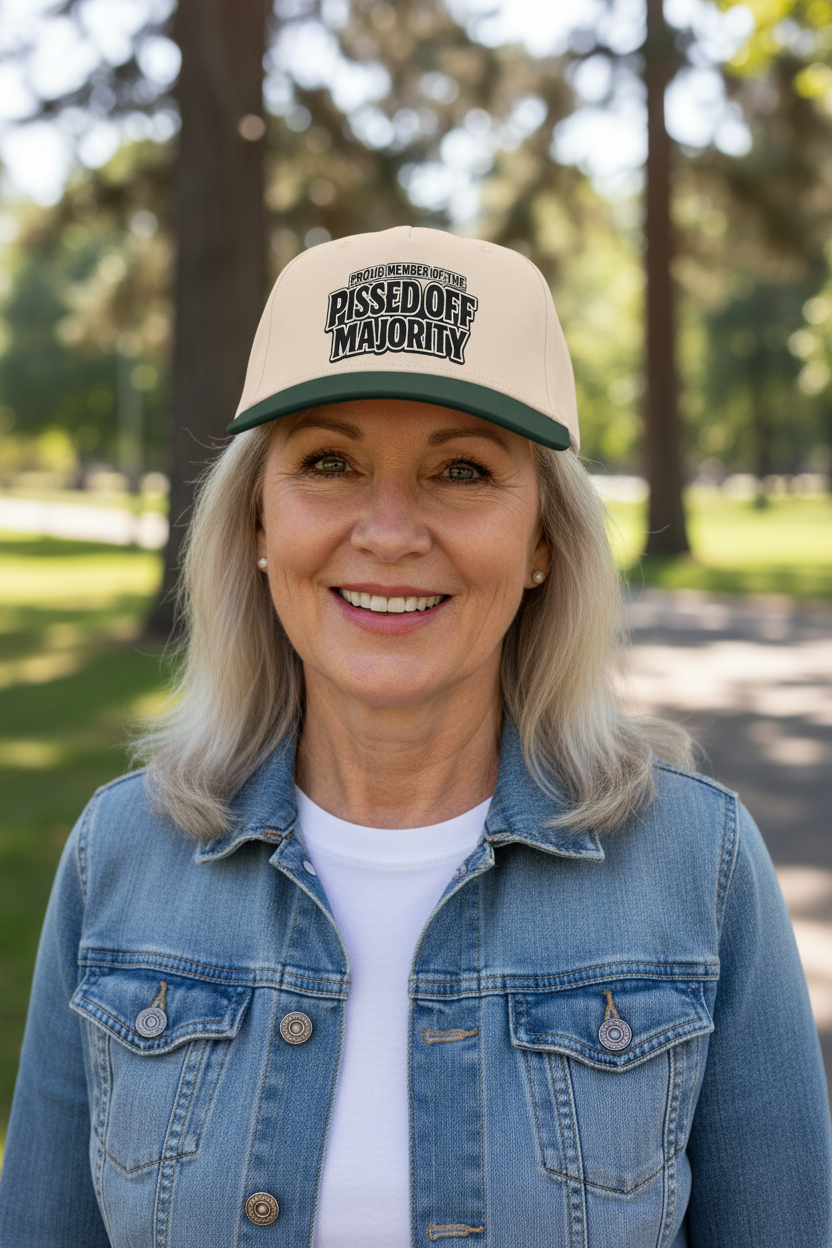 A smiling woman outdoors wearing a beige and green trucker hat with the text 'PISSED OFF MAJORITY' on the front, along with a blue denim jacket over a white shirt.