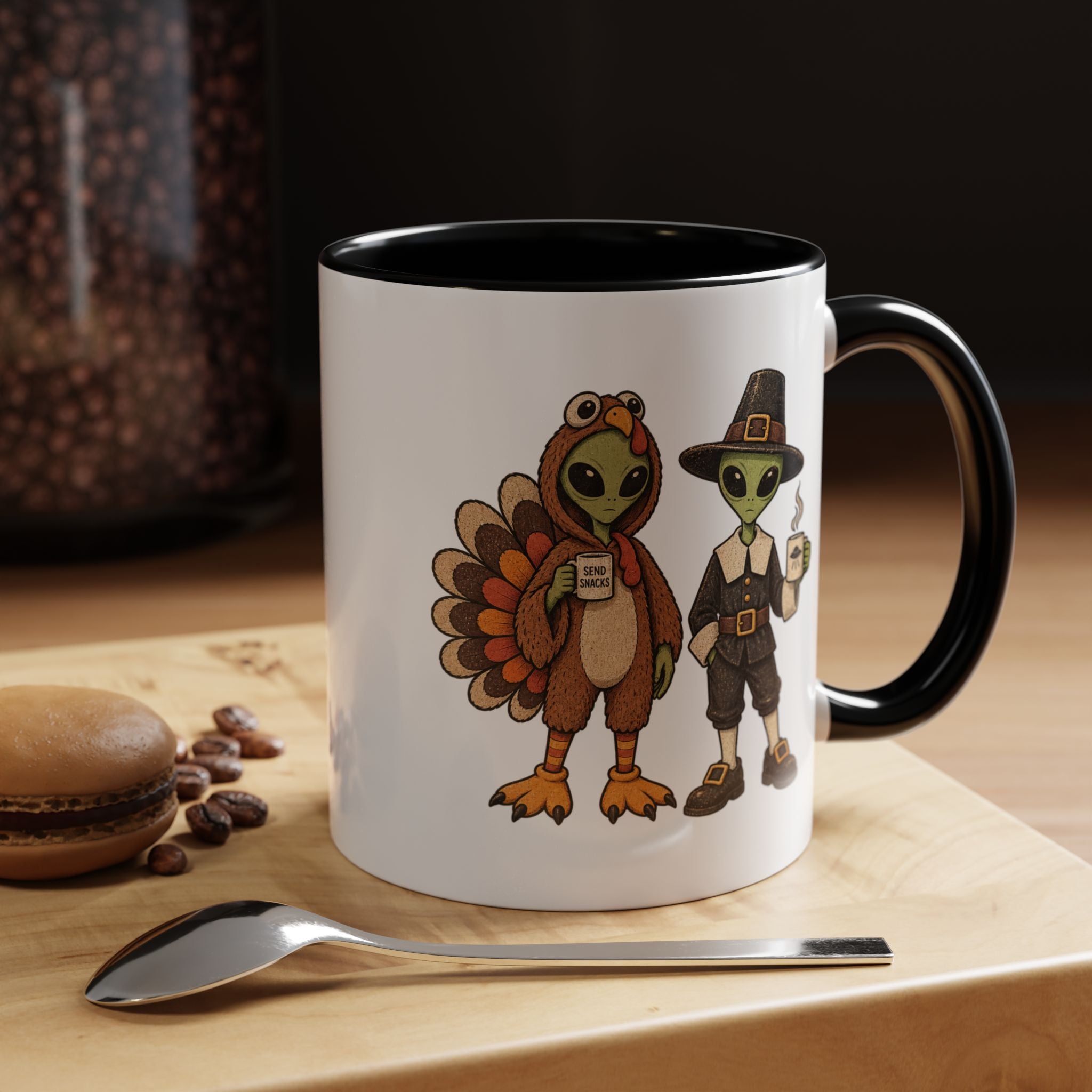 A white ceramic coffee mug with a black interior and handle, featuring a cartoon graphic of a turkey and a pilgrim holding a 'Mug Shot' mug. The mug is set on a wooden board with a spoon and coffee beans in the background