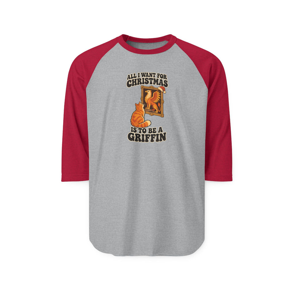 A 3/4 sleeve raglan baseball t-shirt with a heather gray body and dark red sleeves, featuring a graphic of an orange tabby cat in front of a fireplace with the text 'ALL I WANT FOR CHRISTMAS IS TO BE A GRIFFIN'.