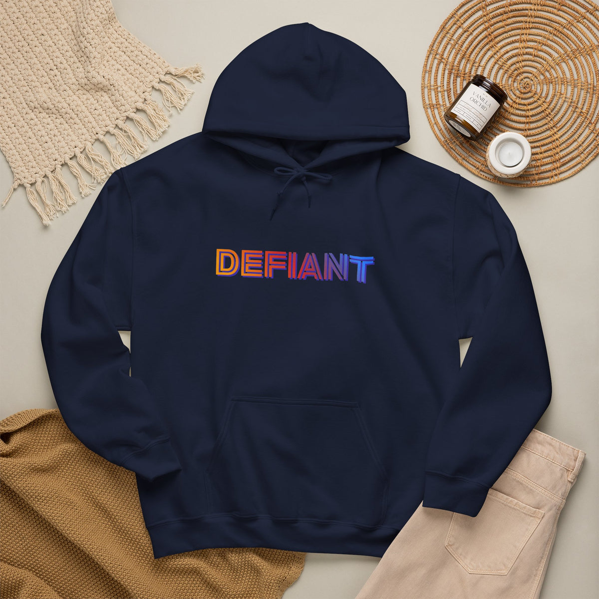 Defiant rainbow text logo graphic hoodie in navy, flat lay styled with a knit blanket, coaster, and jar