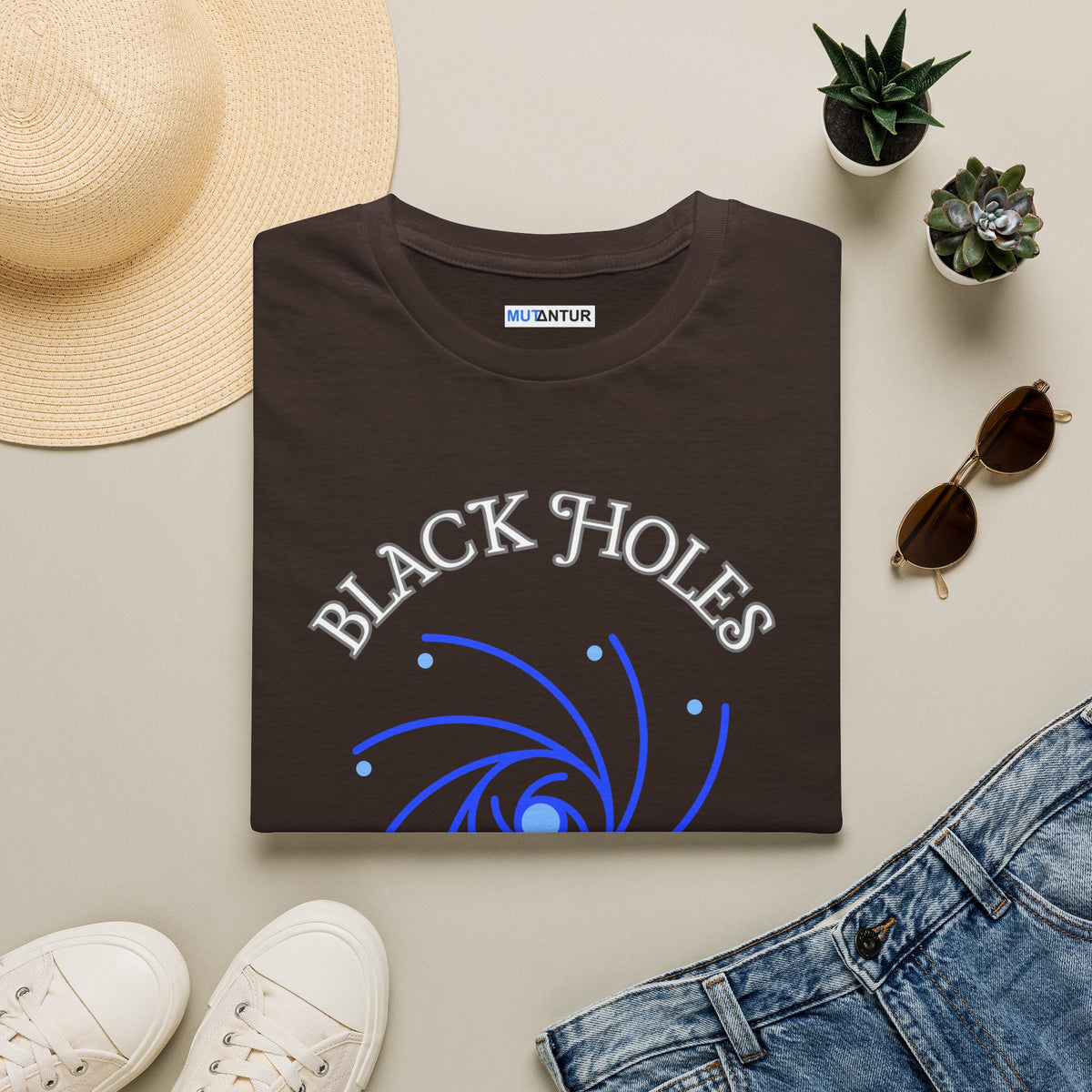 Black Holes Where My Motivation Goes celestial spiral graphic tee in dark brown, folded flat lay styled with a straw hat, succulents, sunglasses, sneakers, and jeans