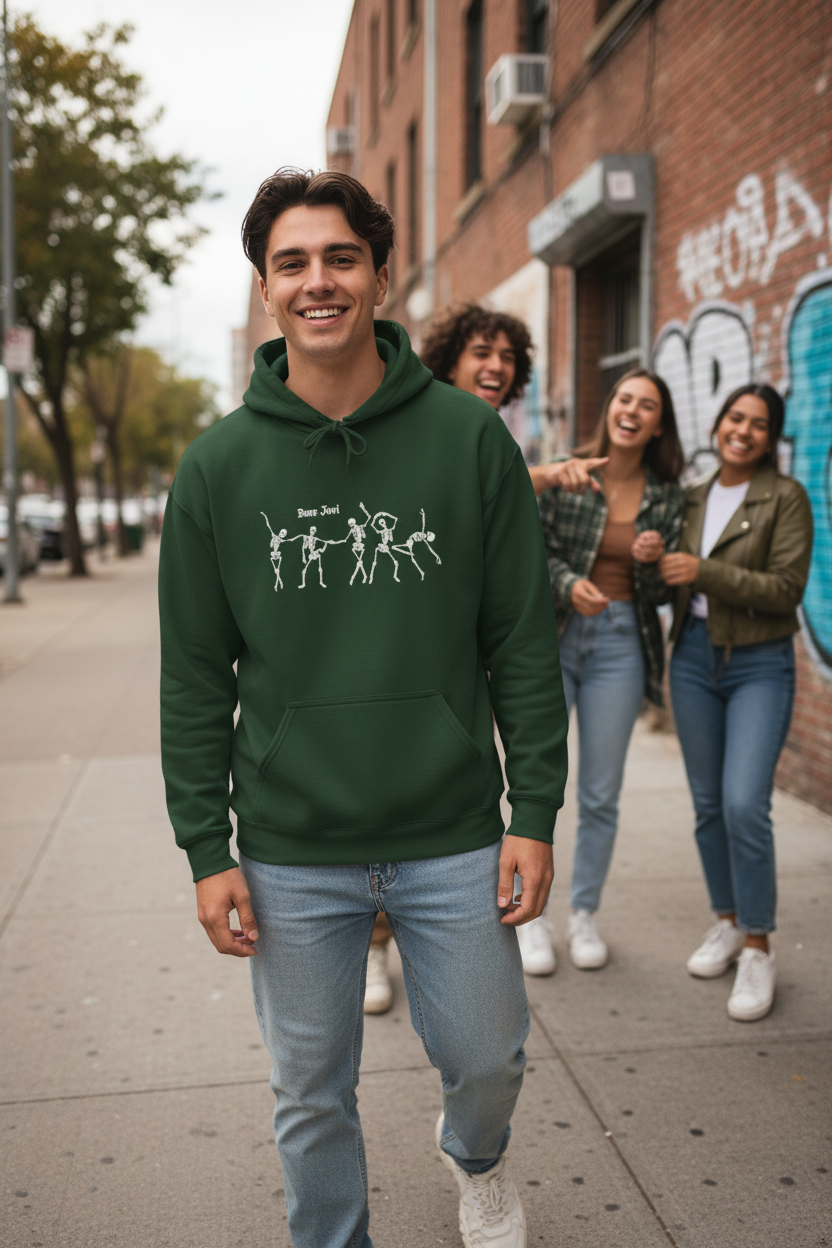 A smiling man in a forest green hoodie with a white graphic walks in front of three laughing friends on an urban sidewalk next to a brick building. He is wearing a green hoodie with dancing skeletons and the works Bone Jovi