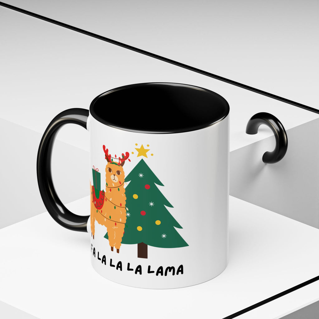 A white ceramic mug with a black handle and black interior, featuring a festive Christmas llama illustration next to a decorated tree and the text 'ALA LA LA LA LAMA'.