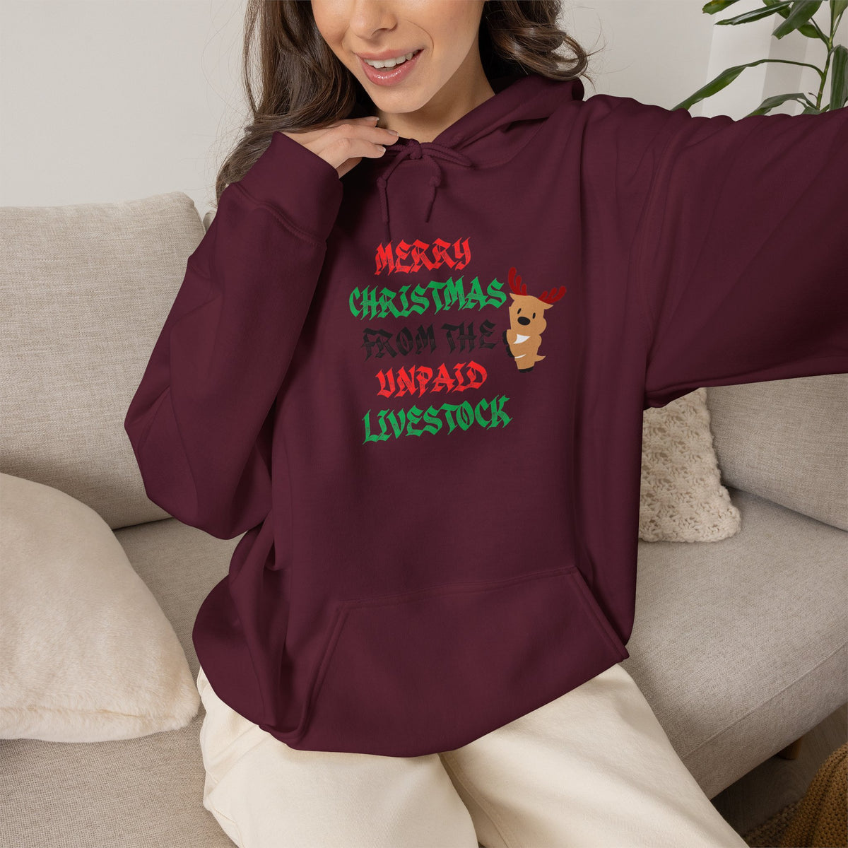 Close-up of a person wearing a maroon  hoodie showing festive red and green words ' Merry Christmas from the Unpaid Livestock' and a cartoon reindeer