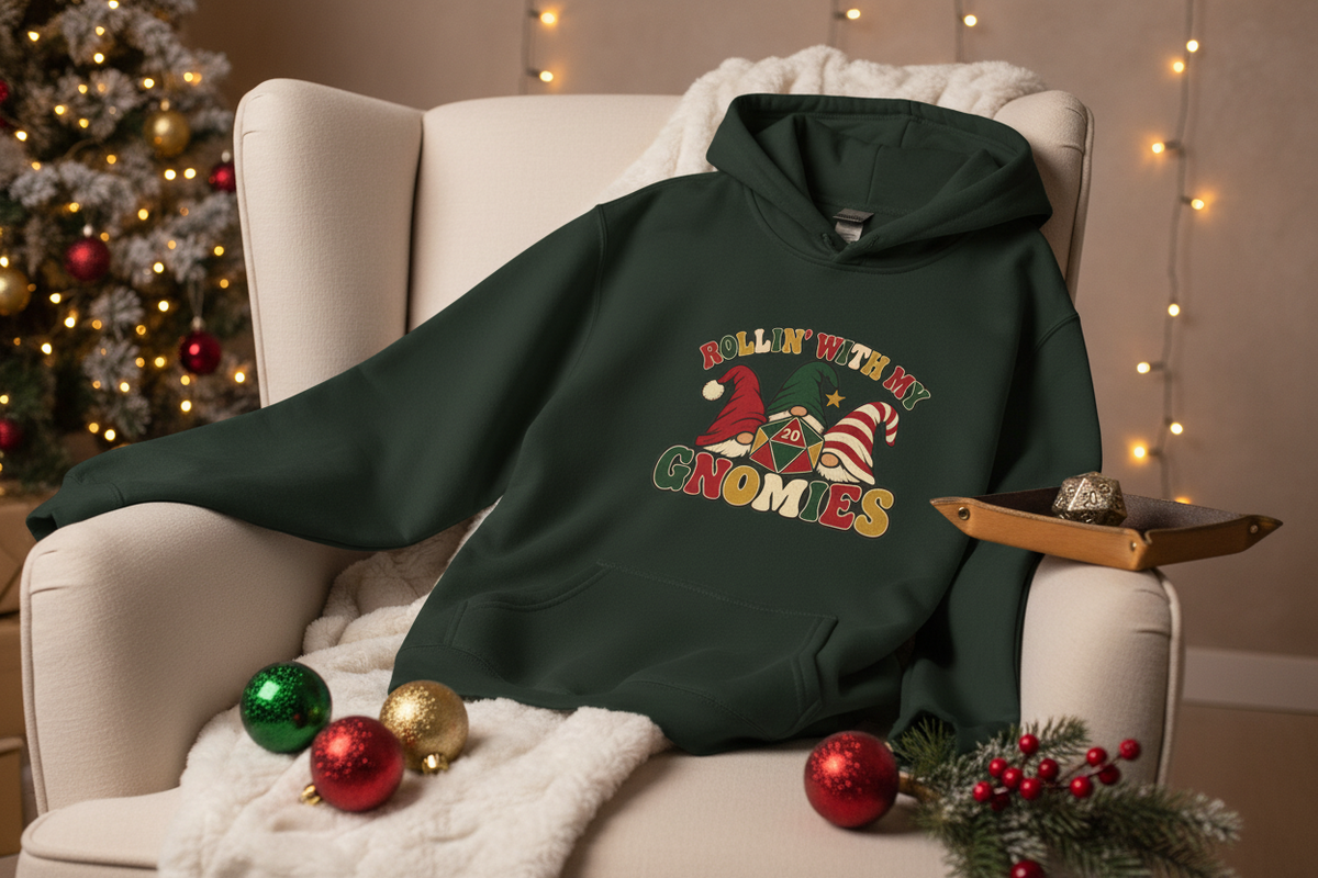 A dark forest green hoodie with a Christmas graphic reading 'ROLLIN WITH MY Gnomes' is styled on a cream armchair with a white throw blanket. The scene is decorated with a Christmas tree, warm string lights, red and gold ornaments, and pine branches.