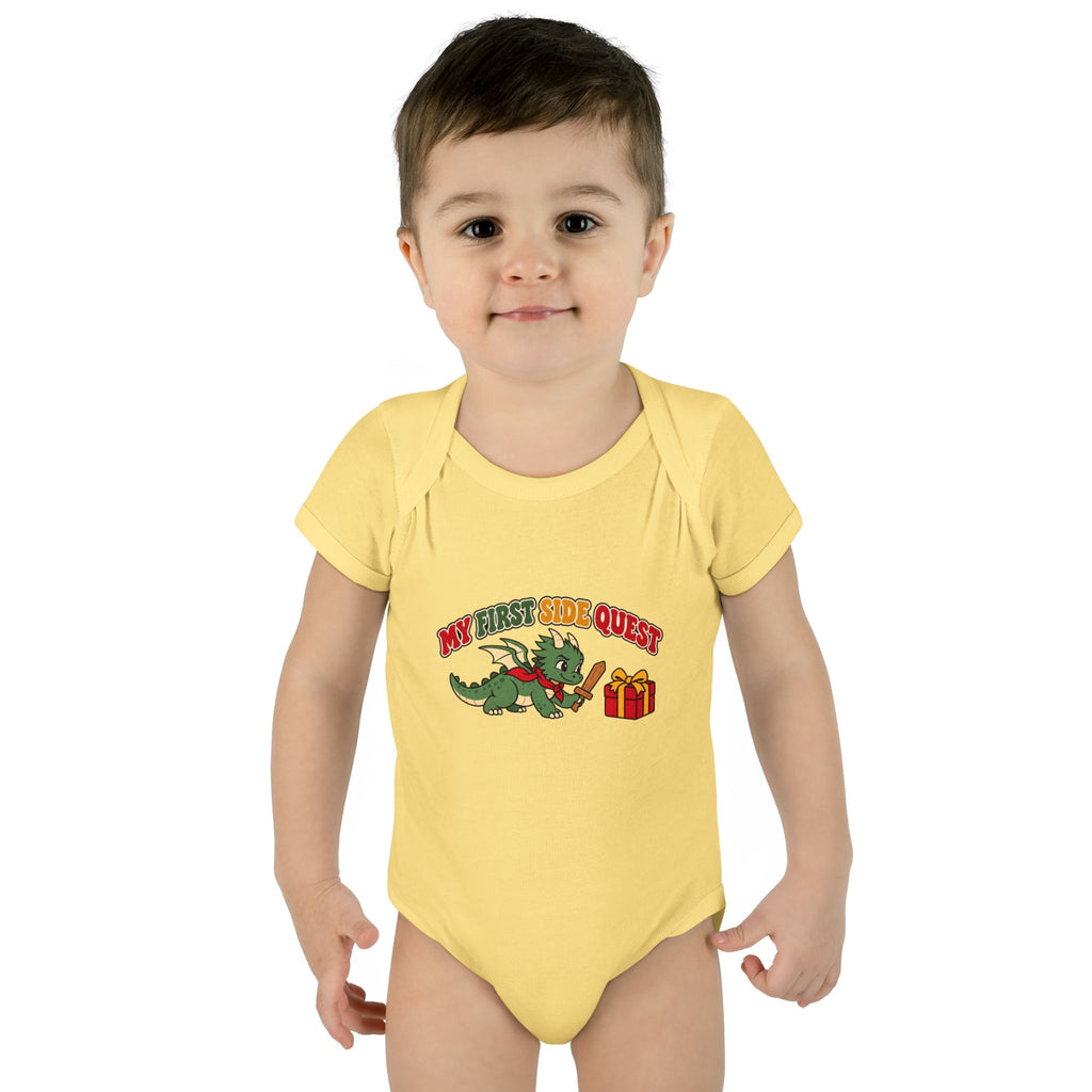 A baby wearing a pale yellow short-sleeve bodysuit with a 'My First Side Quest' cartoon dragon graphic, photographed against a solid white background.