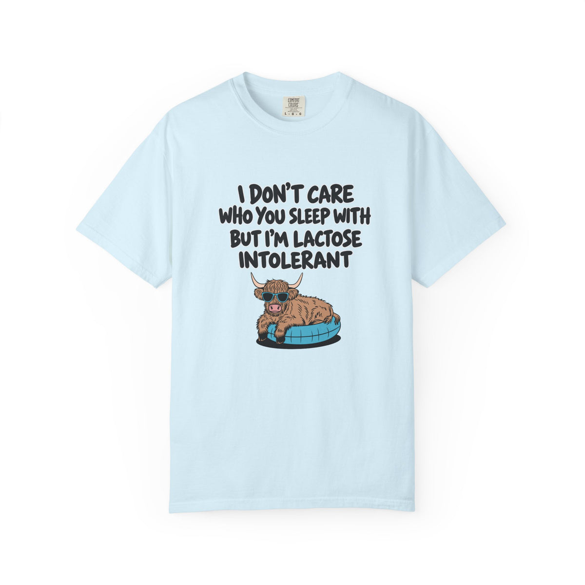 A light blue short-sleeve t-shirt with a humorous graphic on the front. The graphic features the text 'I DON'T CARE WHO YOU SLEEP WITH BUT I'M LACTOSE INTOLERANT' in black lettering above an illustration of a brown highland cow lying on a blue pet bed.