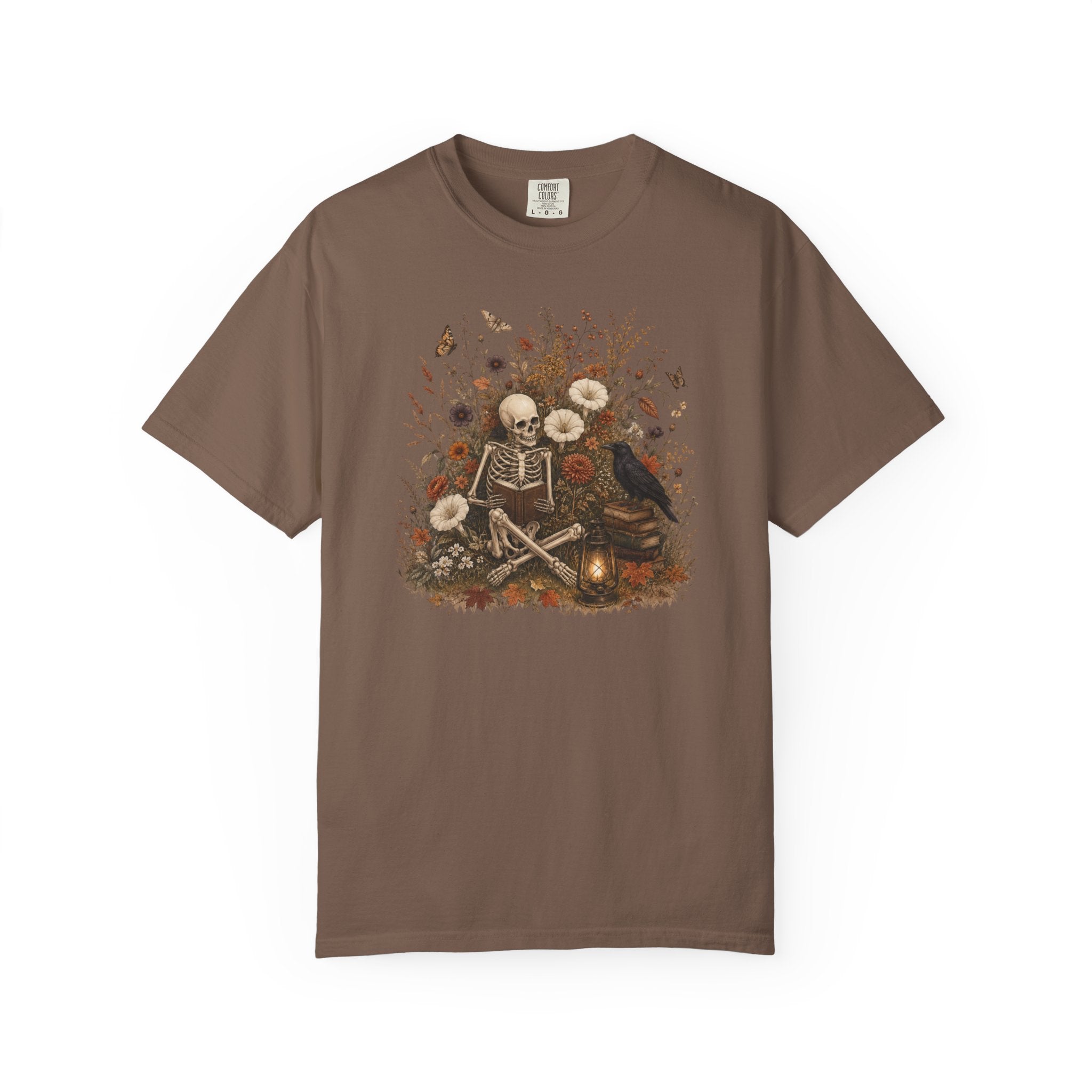 A brown short-sleeve crewneck t-shirt featuring a central graphic of a skeleton sitting cross-legged surrounded by white flowers, a black raven, and autumn leaves.