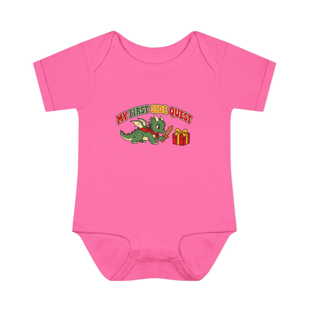 A bright pink short-sleeve baby bodysuit featuring a cartoon graphic of a green dragon wearing a red collar next to a red gift box, with the text 'MY FIRST SIDE QUEST' above it, displayed on a solid white background.