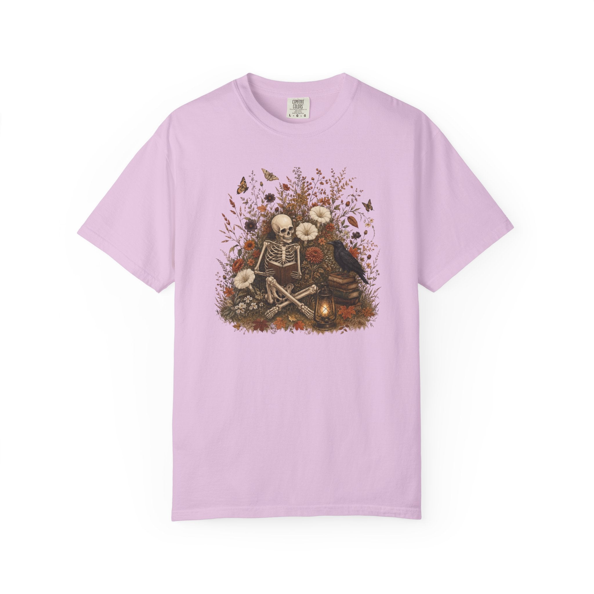 A light purple short-sleeve crewneck t-shirt featuring a central graphic of a skeleton sitting among flowers, butterflies, and a campfire, displayed on a clean white background.