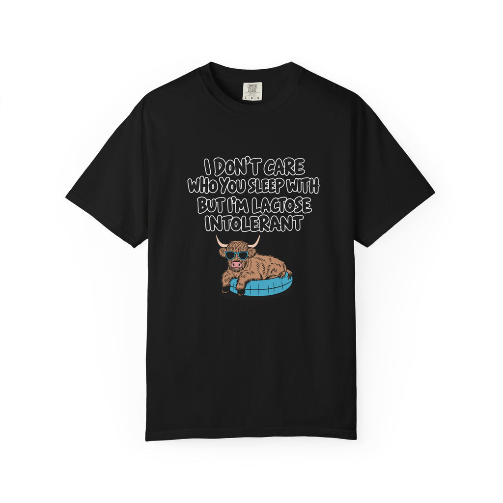 A black short-sleeve crewneck t-shirt featuring a graphic of a Scottish Highland cow lying on a blue blanket with the text 'I DON'T CARE WHO YOU SLEEP WITH BUT I'M LAGOSE INTOLERANT' in white hand-drawn lettering.