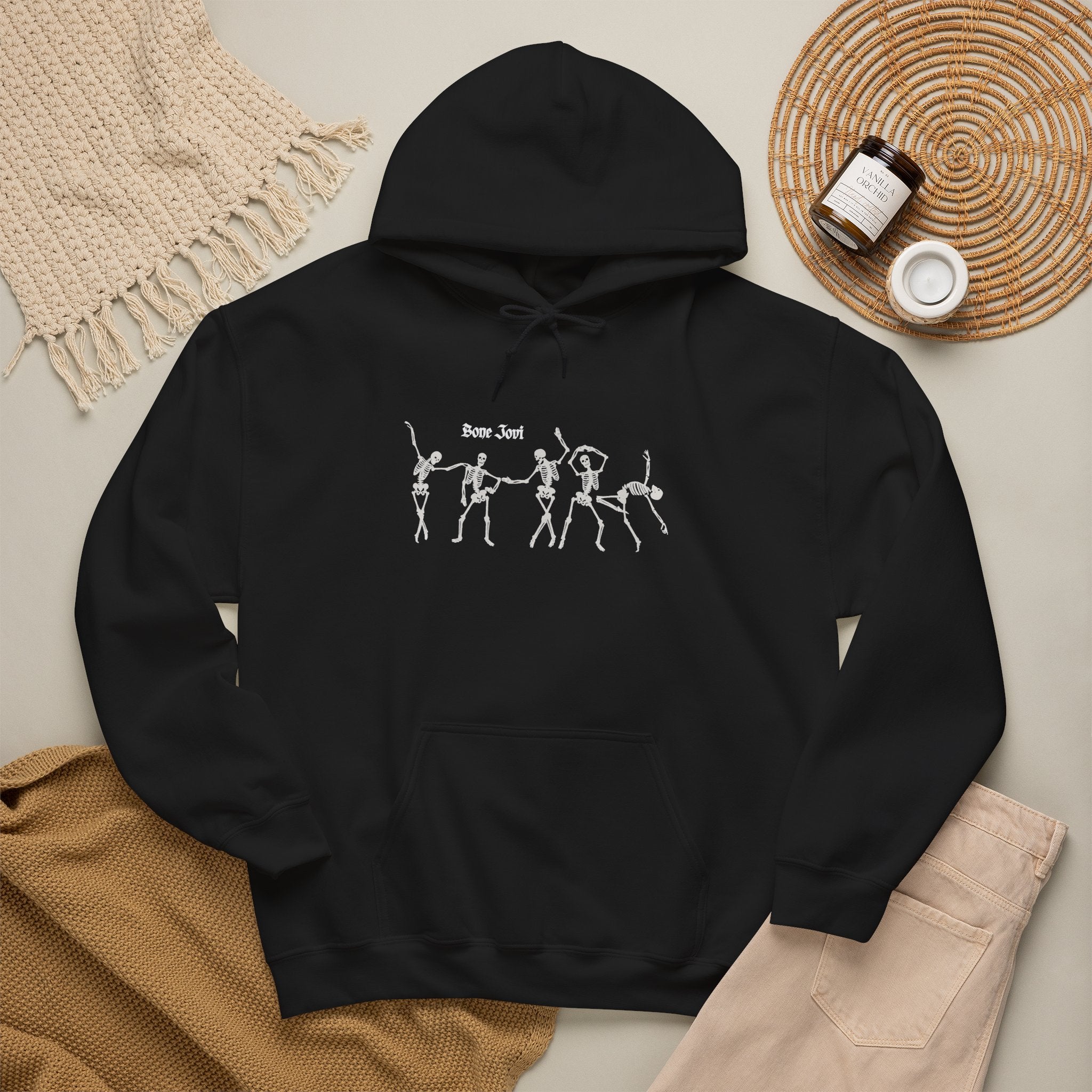 Black hoodie with 6 dancing white skeletons with the words Bone Jovi against a tan background with a =sweater and a candle