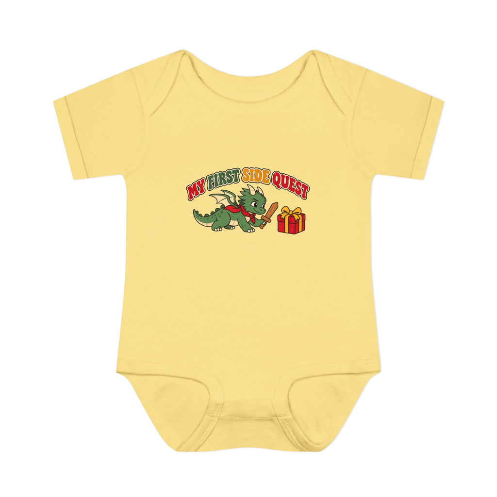 A pale yellow short-sleeve baby bodysuit with a colorful graphic on the chest showing a green cartoon dragon, a red gift box, and the text 'MY FIRST SIDE QUEST'.