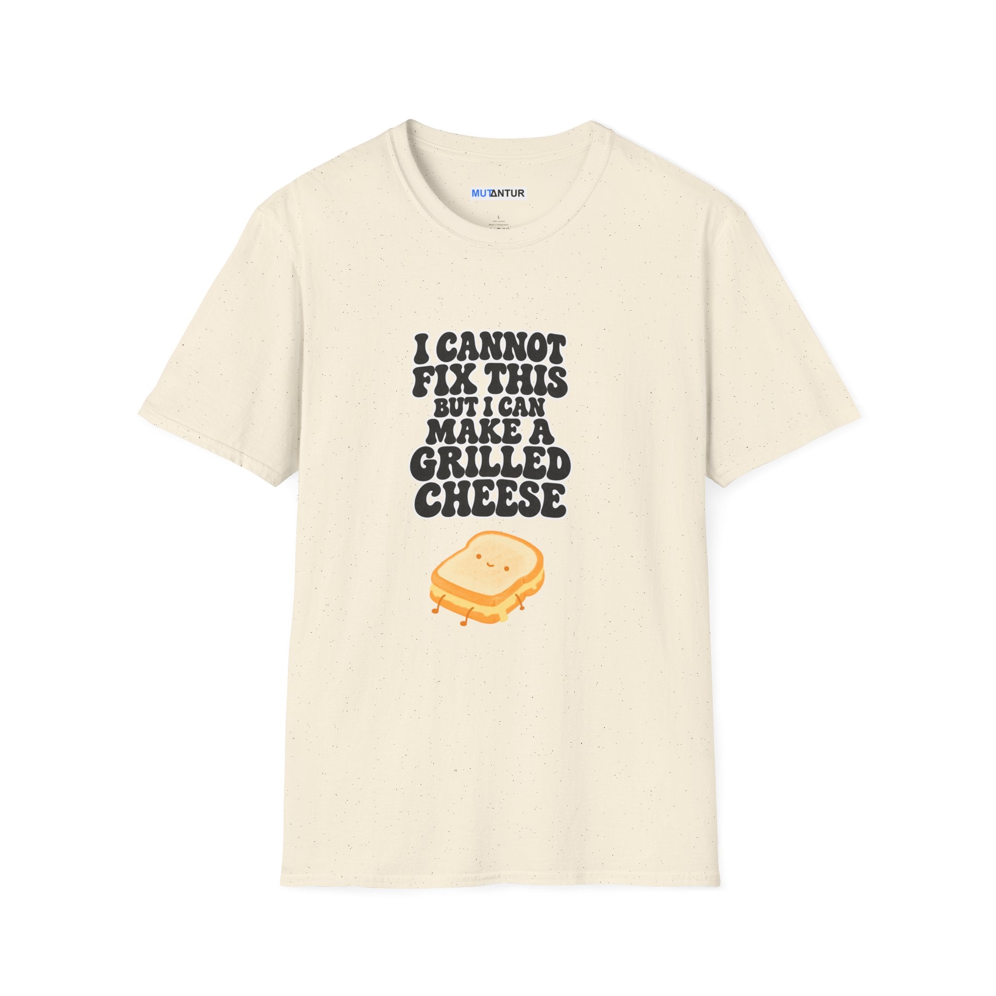 A beige crewneck short-sleeve t-shirt with a graphic on the front that reads 'I CANNOT FIX THIS BUT I CAN MAKE A GRILLED CHEESE' in a white and black bubbly font, above a cartoon grilled cheese sandwich. The shirt is displayed flat against a solid white background