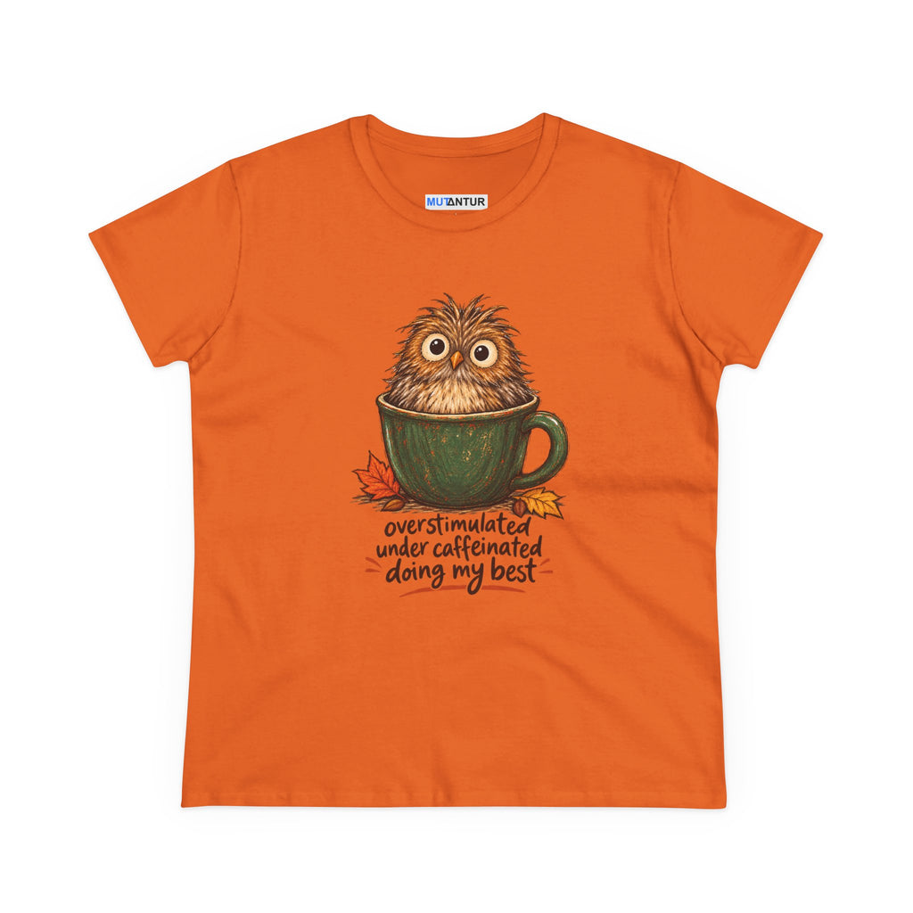 An orange short-sleeve graphic t-shirt on a white background. The shirt features a cartoon illustration of a fluffy brown owl sitting inside a green mug, with autumn leaves and the text 'overstimulated under caffeinated doing my best' printed below.
