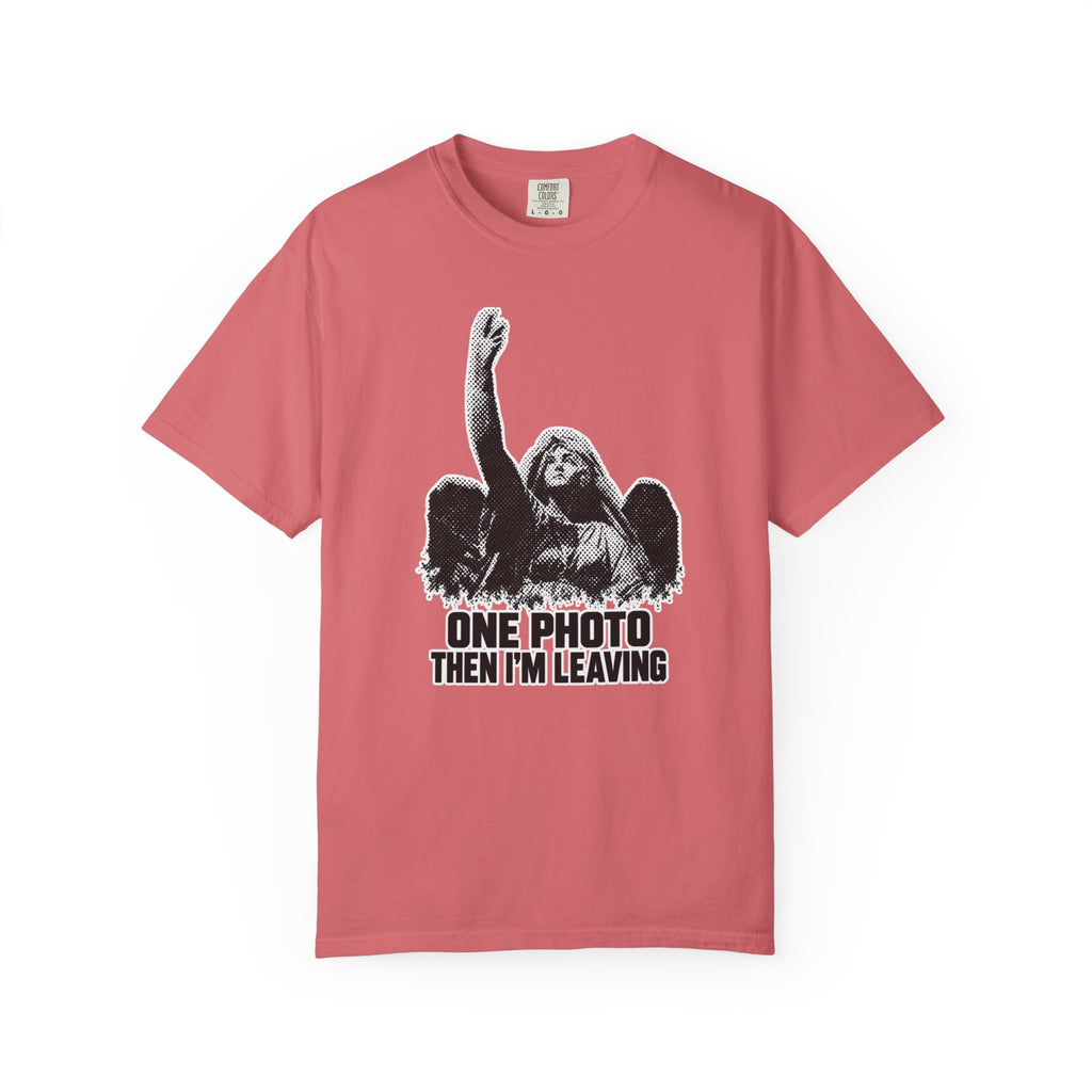 A pink short-sleeve crewneck t-shirt featuring a black and white graphic of a winged angel with a raised hand, above the text 'ONE PHOTO THEN I'M LEAVING' in black block letters.