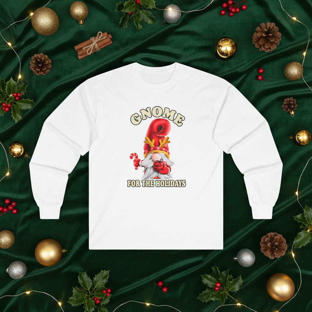 A white long-sleeve crewneck sweatshirt with a festive gnome graphic, displayed in a flat-lay holiday setting on a dark green satin background surrounded by ornaments, pinecones, and lights.