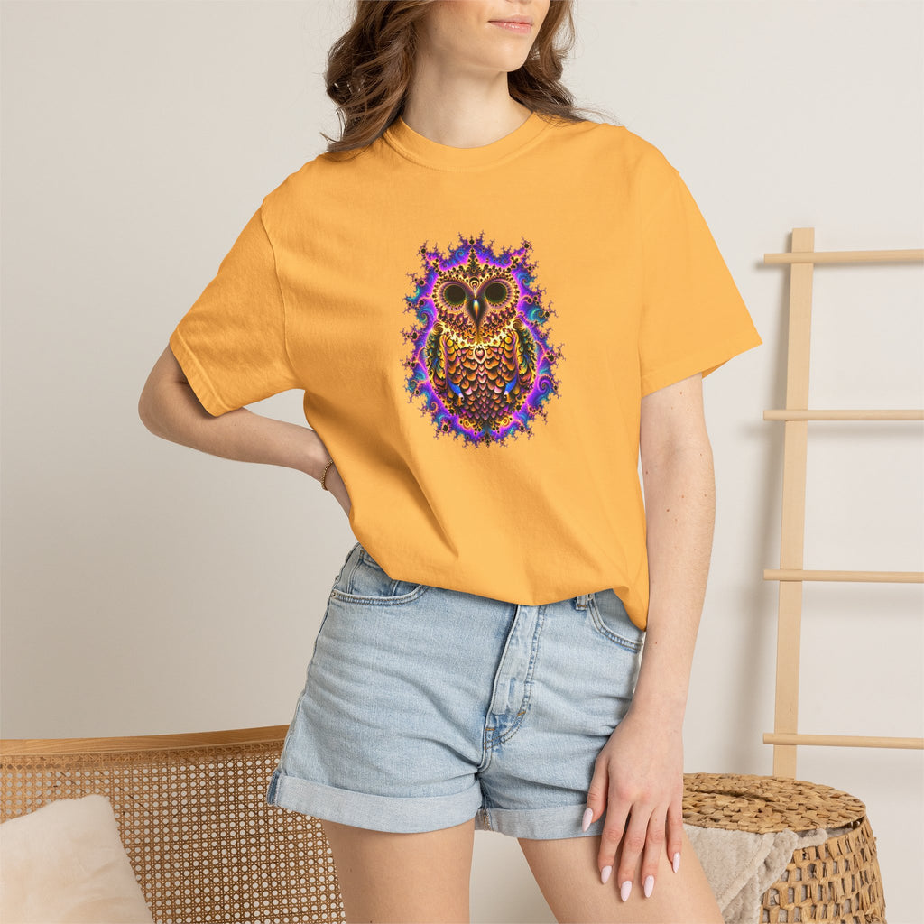 A woman wearing a mustard yellow t-shirt with a colorful, detailed owl graphic on the chest, paired with light blue denim shorts in a cozy indoor settin