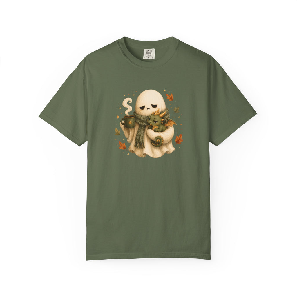 An olive green short-sleeve crewneck t-shirt featuring a central graphic of a cute cartoon ghost wearing a brown knit sweater and scarf, holding a mug, surrounded by small orange autumn leaves.