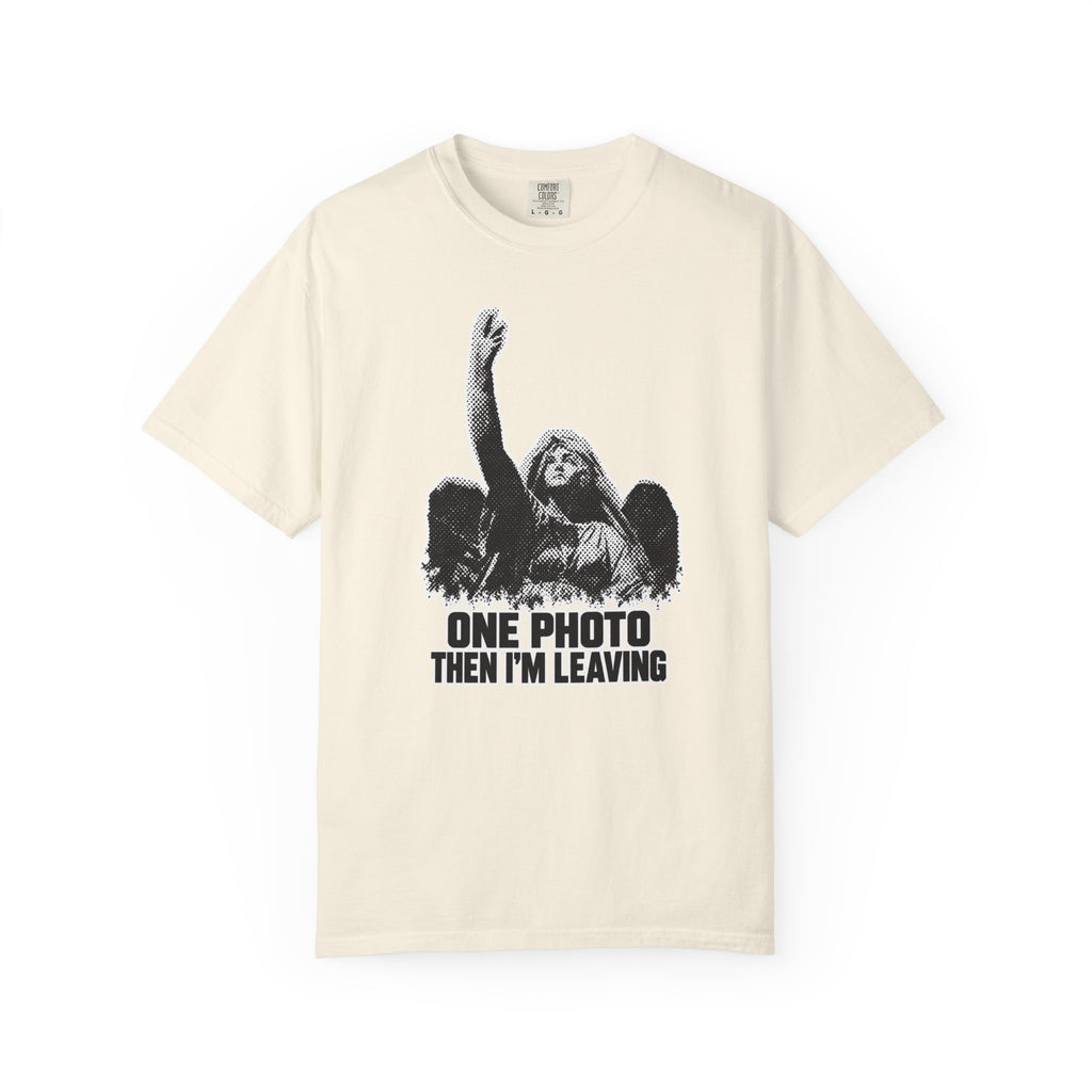 A beige  short-sleeve crewneck t-shirt in a  featuring a black and white graphic of an angel with one arm raised and the text 'ONE PHOTO THEN I'M LEAVING' printed below.
