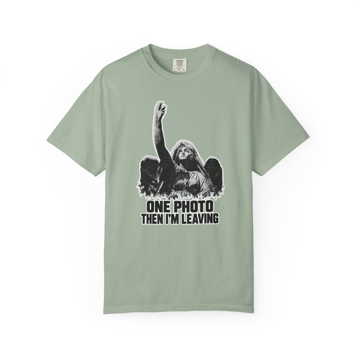A sage green short-sleeve t-shirt with a black-and-white graphic of a woman raising her fist, accompanied by the text 'ONE PHOTO THEN I'M LEAVING'.