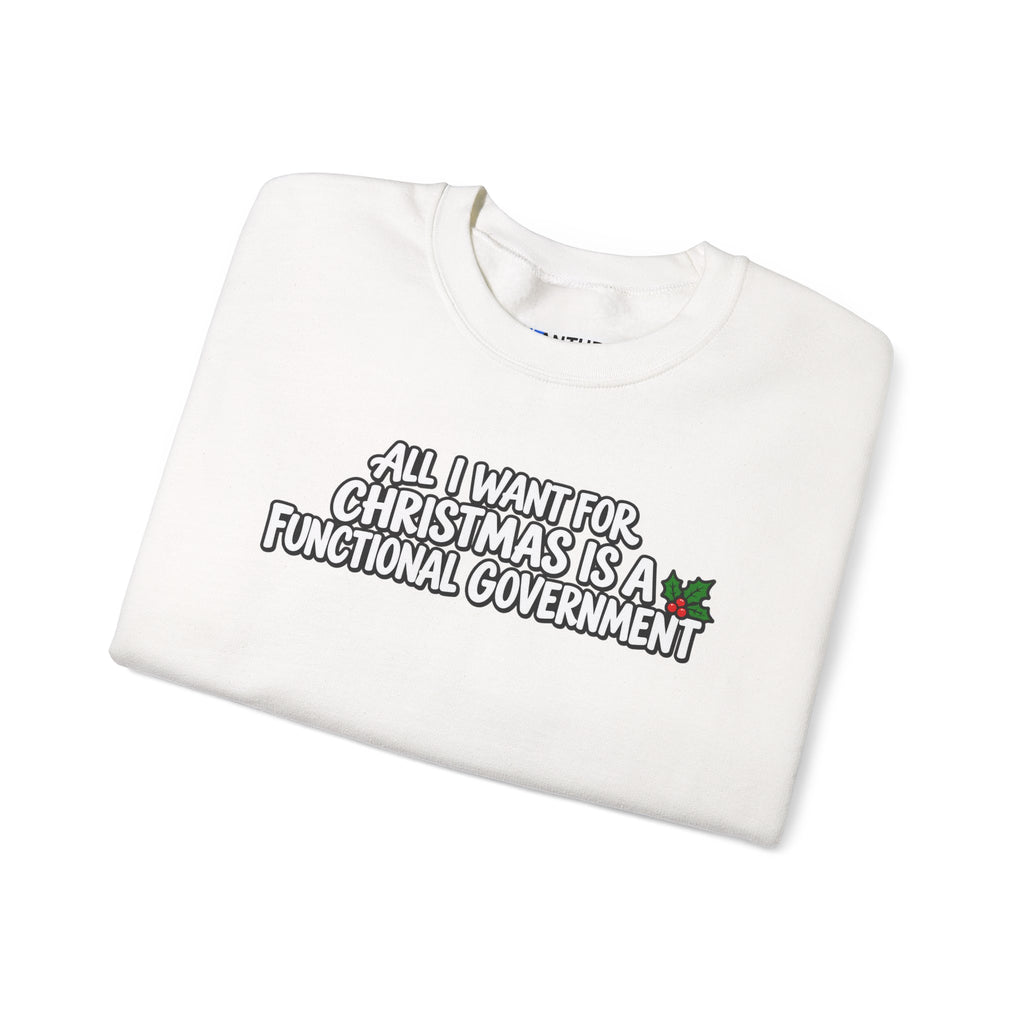 A folded white crewneck sweatshirt with a humorous graphic printed on the front. The graphic features the text 'ALL I WANT FOR CHRISTMAS IS A FUNCTIONAL GOVERNMENT' in a stylized black and white font, accented with a small green holly leaf with red berries on the right side